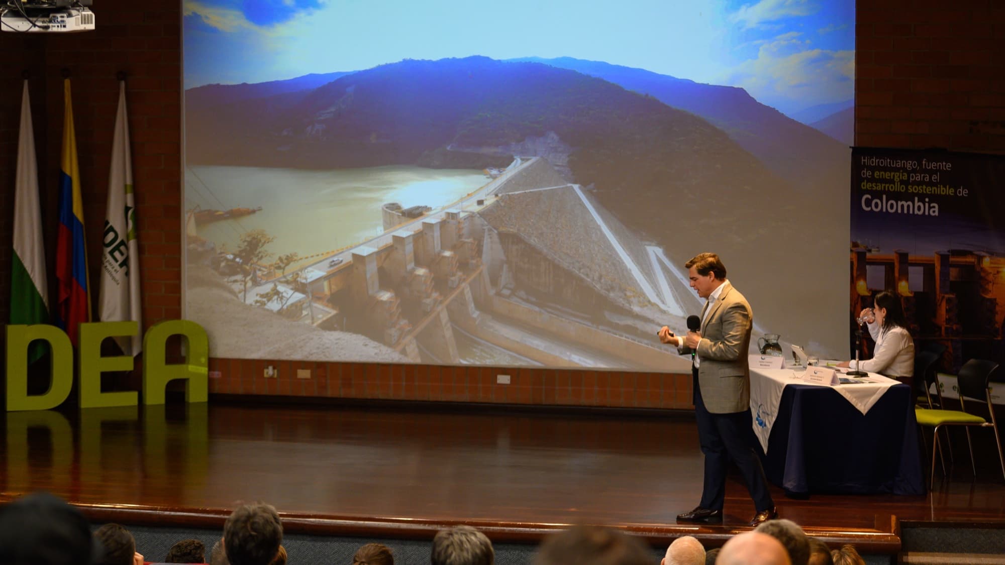 Alejandro Arbeláez expone ante un auditorio con una imagen de la presa de Hidroituango proyectada detrás