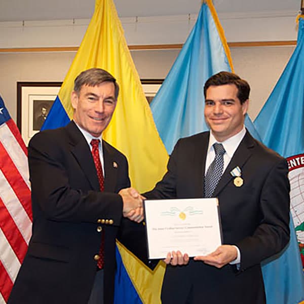 Alejandro Arbeláez recibe un reconocimiento académico frente a las banderas de Colombia y Estados Unidos