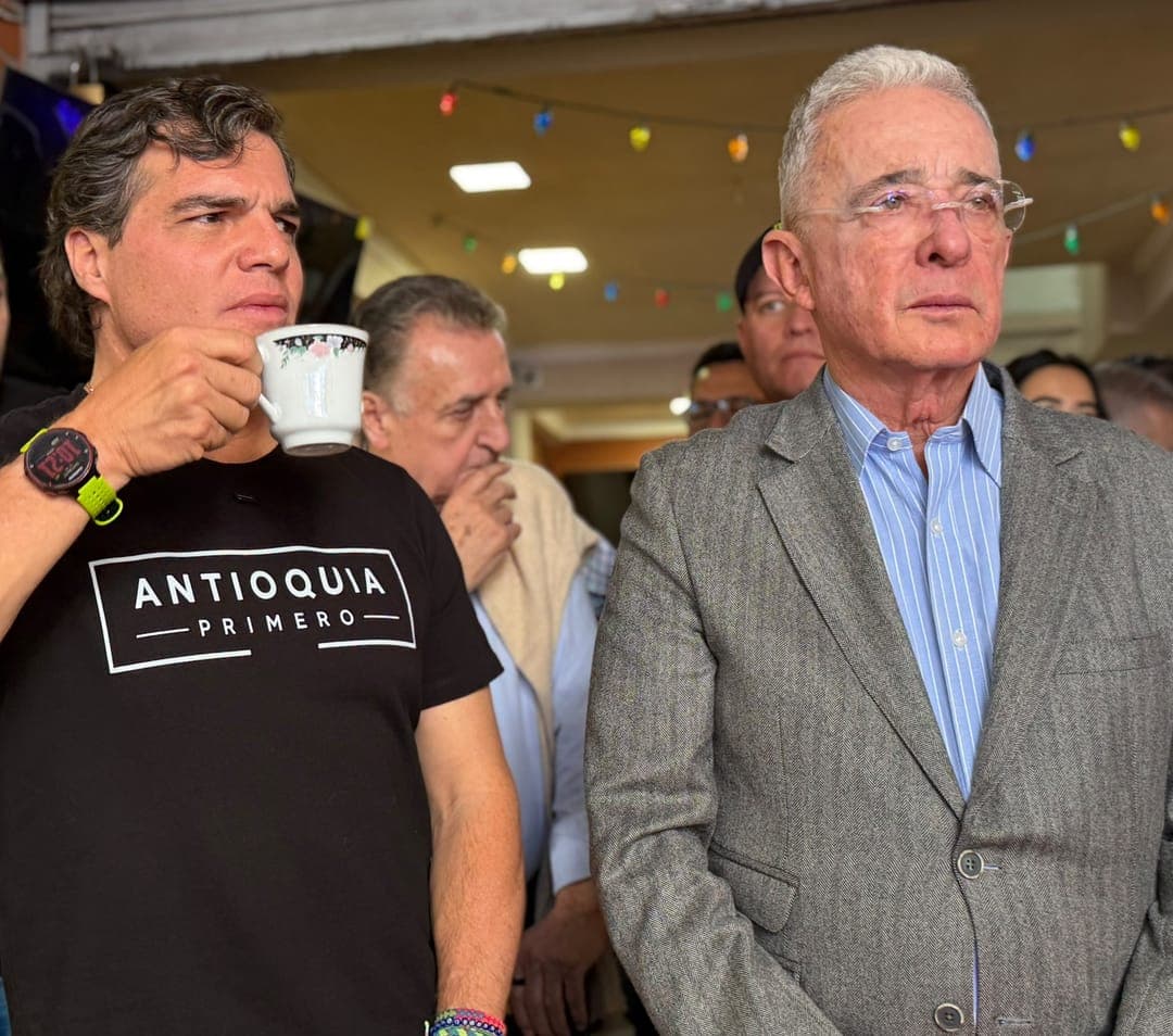 Alejandro Arbeláez A., con camiseta «Antioquia Primero» y un pocillo de café, de pie junto a Álvaro Uribe Vélez